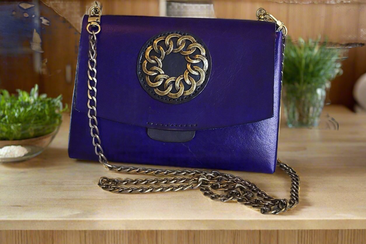 Blue purse with black pocket and burnished gold accents and curb chain strap.