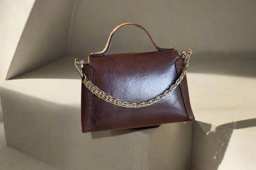 Backside of a small brown leather handbag with optional gold chain attached