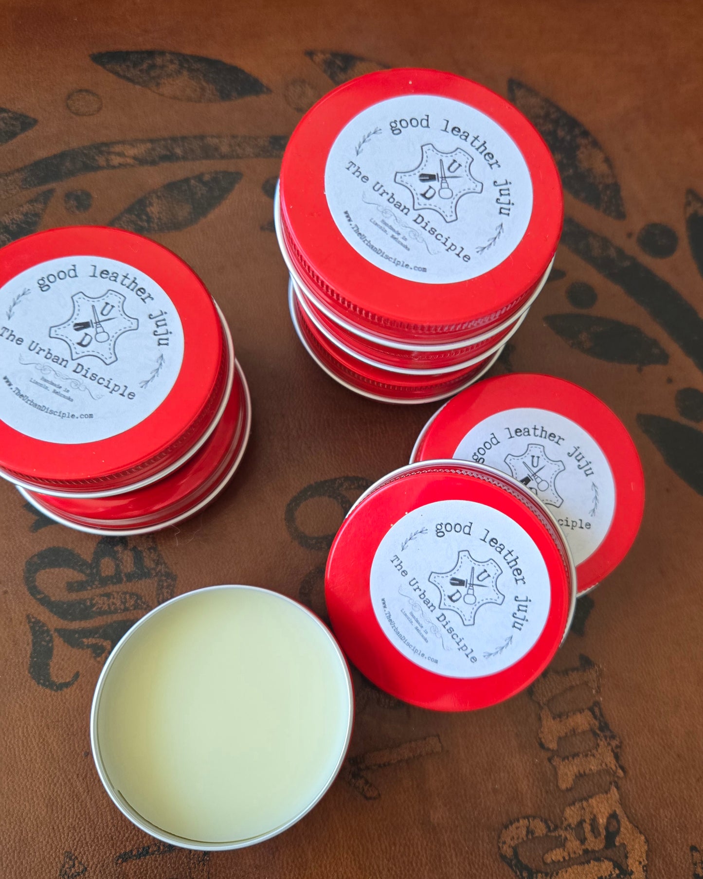 Red tins with white labels containing a yellow substance on a brown surface.