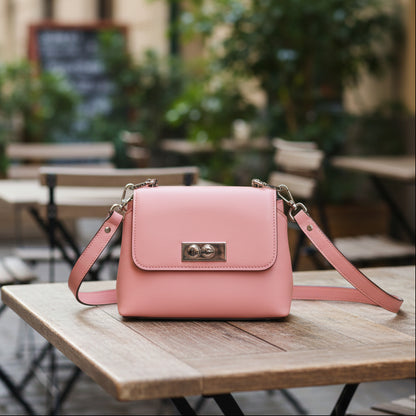 Pink handbag with a strap on a outdoor cafe table.
