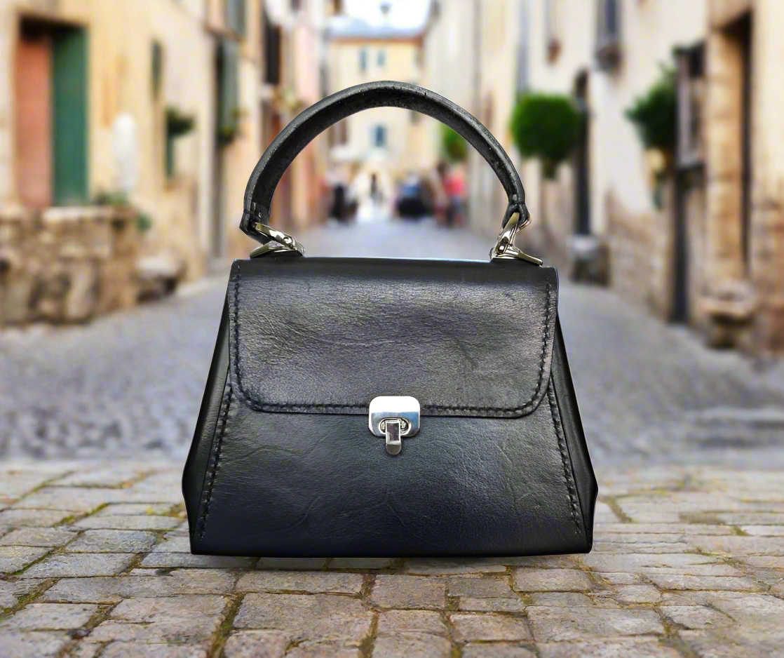 small black leather handbag with silver hardware sitting on a low brick wall.