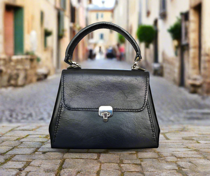 small black leather handbag with silver hardware sitting on a low brick wall.